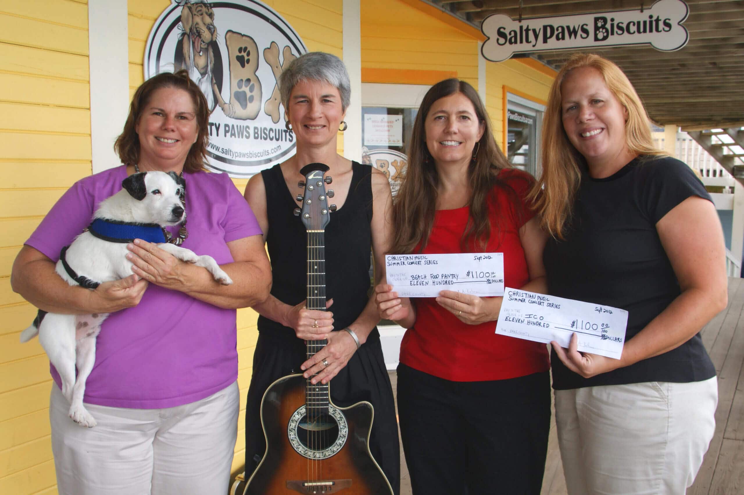 Kim Kalman, woman with guitar, at Salty Paws Biscuits event with women and dogs.