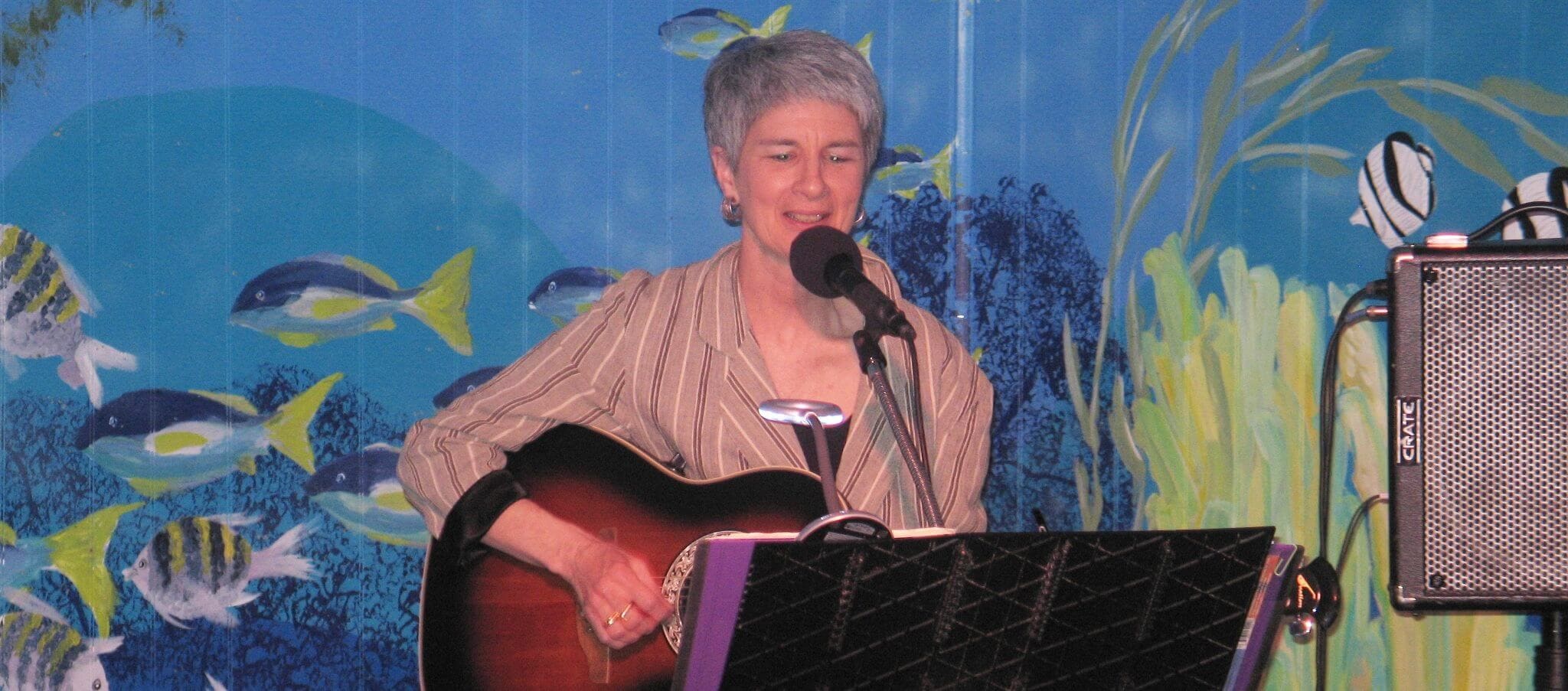 Kim Kalman singing and playing guitar at a vibrant underwater-themed event.
