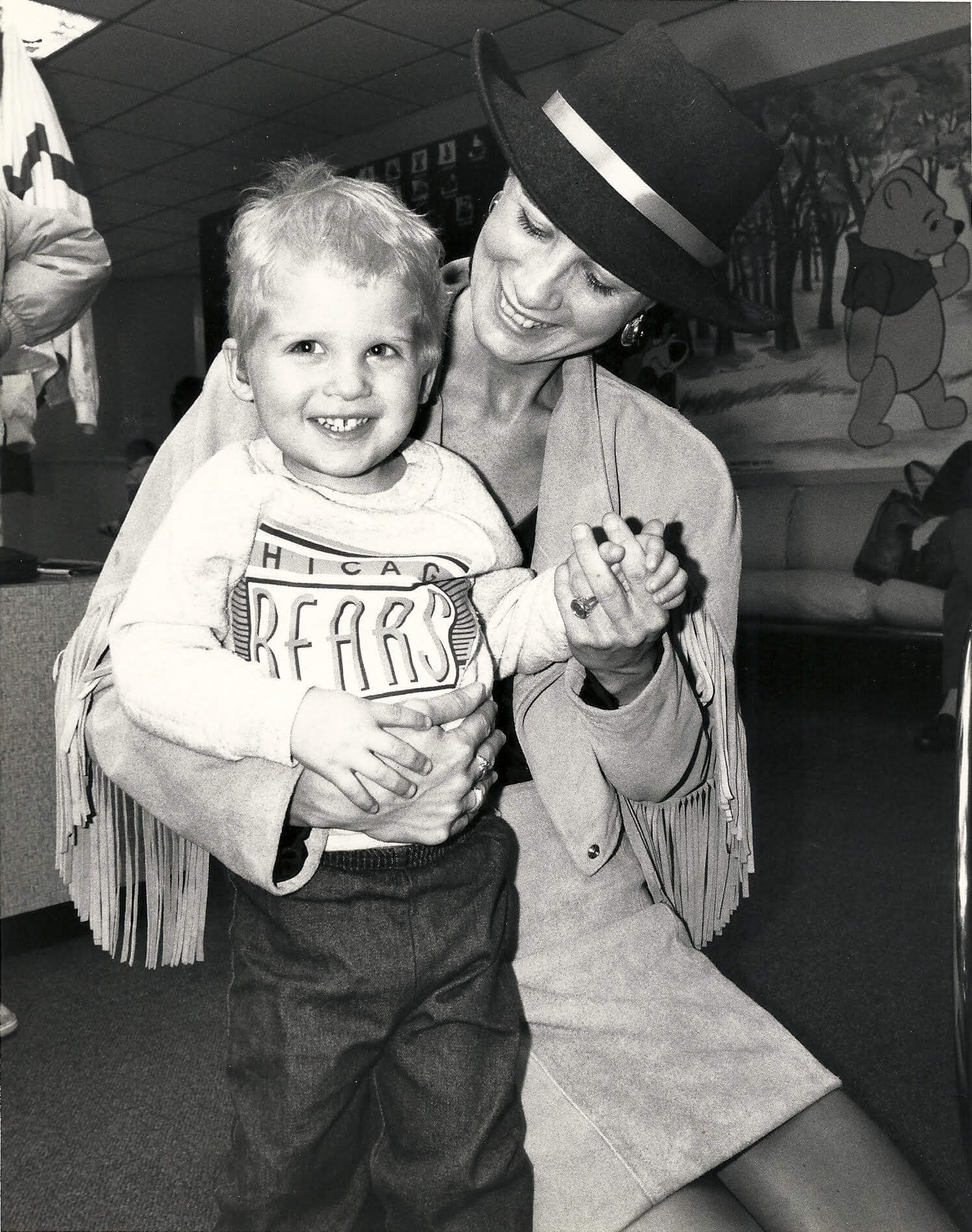 Smiling woman with a hat holding a cheerful child, both enjoying a fun moment together.