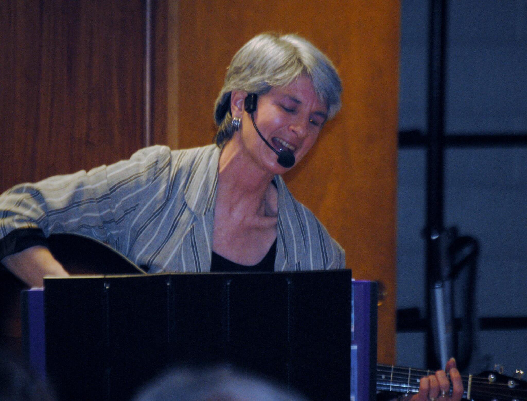 Performing singer-songwriter Kim Kalman with guitar and microphone on stage.